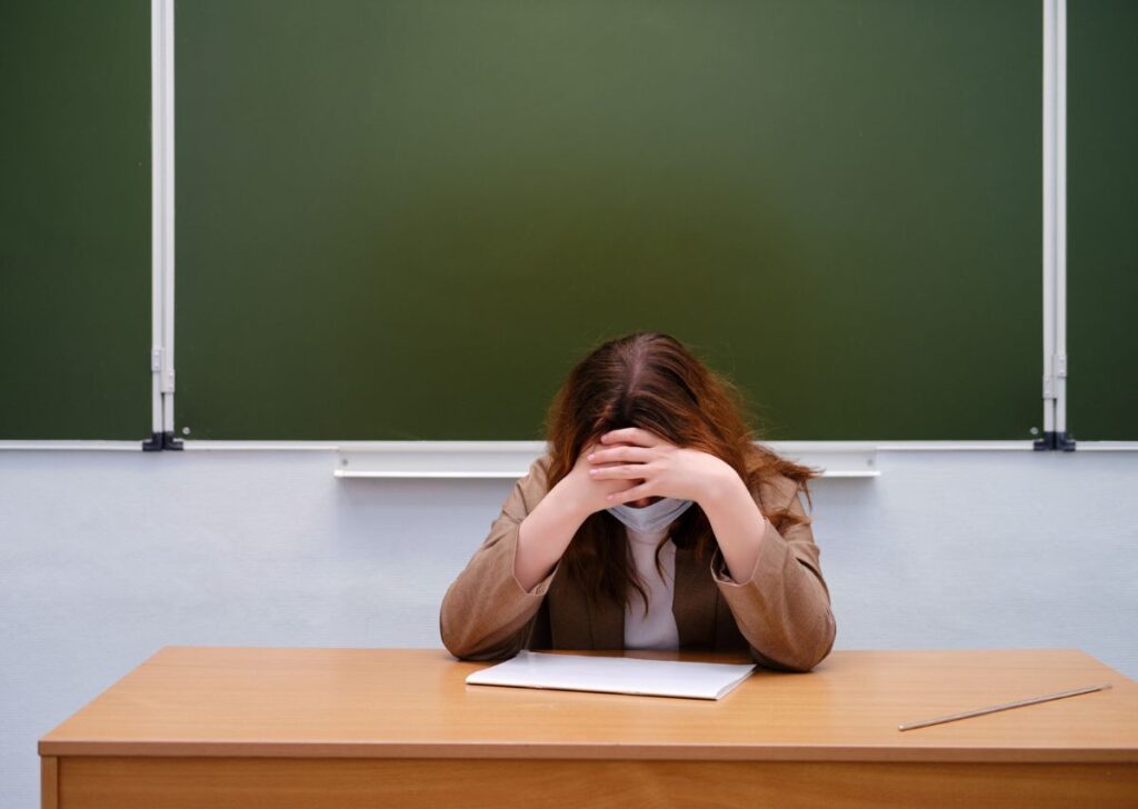 Junge verzweifelte Lehrerin stützt ihren Kopf mit ihren verschränkten Händen